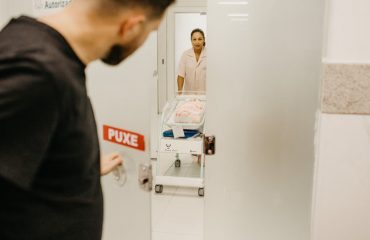 A man opens a door to see his newborn in a hospital room attended by a nurse.